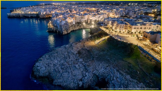 Veduta Aerea Notturna Panoramica del Largo Gelso e del Suggestivo Centro Storico di Polignano a Mare Arroccato sulla Scogliera