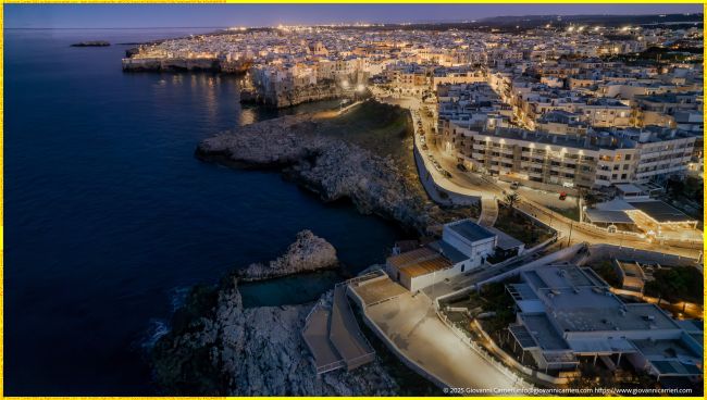Vista Aerea Panoramica del Lungomare Domenico Modugno e del Centro Storico di Polignano a Mare Illuminati di Sera
